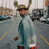 Man in a denim jacket and hat standing on a city street