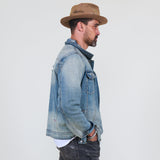 Man wearing a denim jacket and brown hat against a plain background