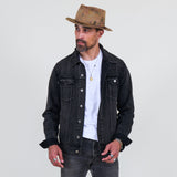 Man wearing a black denim jacket, white shirt, and brown hat on a light gray background