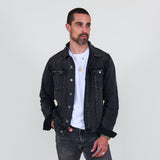 Man wearing a black denim jacket and jeans against a plain background