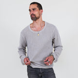 Man wearing a gray long sleeve tee and dark jeans standing against a white background