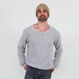 Man wearing a gray long sleeve tee and dark jeans standing against a white background