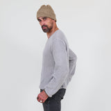 Man wearing a gray long sleeve tee and dark jeans standing against a white background