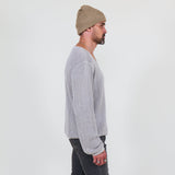 Man wearing a gray long sleeve tee and dark jeans standing against a white background