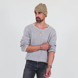 Man wearing a gray long sleeve tee and dark jeans standing against a white background