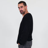 Man wearing a black long sleeve tee and gray jeans standing against a white background