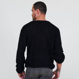 Man wearing a black long sleeve tee and gray jeans standing against a white background