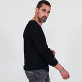 Man wearing a black long sleeve tee and gray jeans standing against a white background