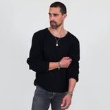 Man wearing a black long sleeve tee and gray jeans standing against a white background