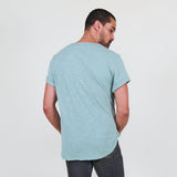 Man wearing a teal t-shirt and dark jeans standing against a white background