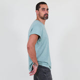 Man wearing a teal t-shirt and dark jeans standing against a white background
