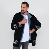 Man wearing a black cardigan with white patterns, white shirt and gray jeans on a white background