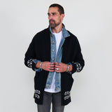 Man wearing a black cardigan with white patterns, white shirt and gray jeans on a white background