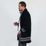 Man wearing a black cardigan with white patterns, white shirt and gray jeans on a white background