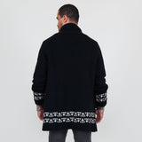 Man wearing a black cardigan with white patterns, white shirt and gray jeans on a white background