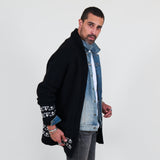 Man wearing a black cardigan with white patterns, white shirt and gray jeans on a white background