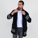 Man wearing a black cardigan with white patterns, white shirt and gray jeans on a white background