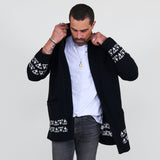 Man wearing a black cardigan with white patterns, white shirt and gray jeans on a white background