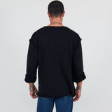 Man wearing a black sweater and blue jeans standing against a white background