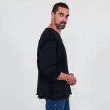 Man wearing a black sweater and blue jeans standing against a white background