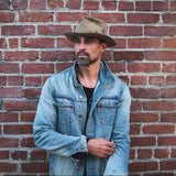 Man wearing a denim jacket and hat standing against a brick wall