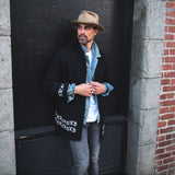 Man standing against a brick wall wearing a black jacket and hat.