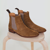 Pair of brown suede boots on a light wooden stool against a white background