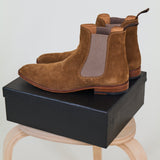 Pair of brown suede boots on a light wooden stool against a white background